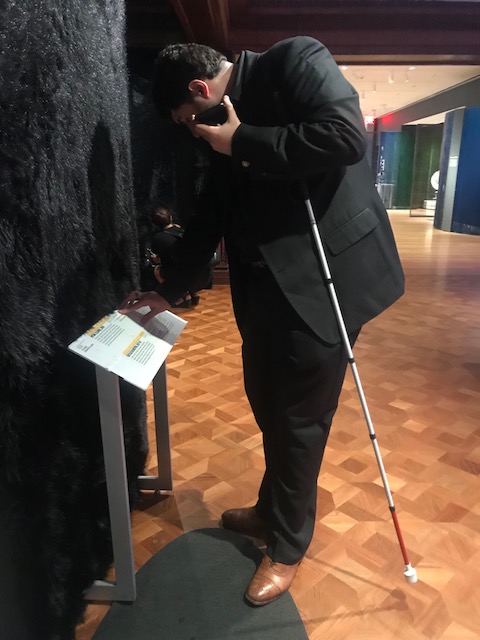 Sina leans slightly down to touch a small metal stand with his right hand while also holding his phone to his left ear.