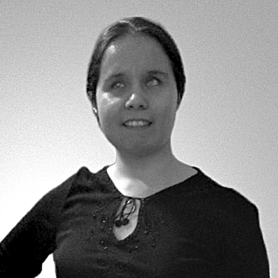 A headshot of a woman with light skin, and straight dark hair parted in the middle and pulled back, shown from mid-torso up. She has a slight smile and cloudy eyes. Her blouse is black, long-sleeved, embellished with embroidery, and features a keyhole neckline with a tassel tie, laying just below her collarbone.